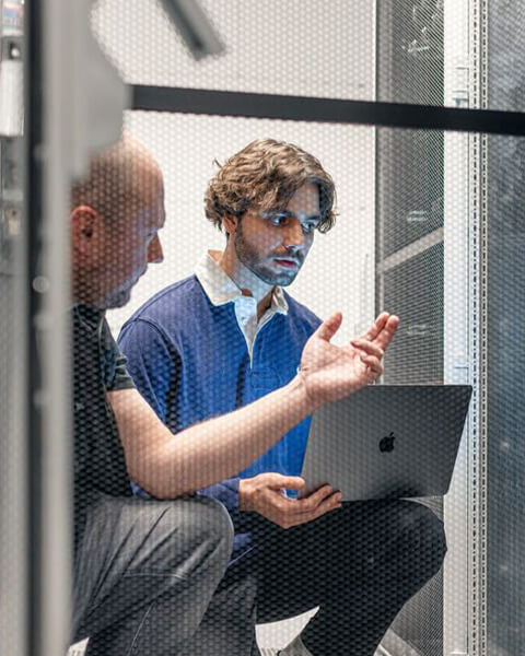 Zwei Männer diskutieren sitzend vor einem Server in einem Serverraum.