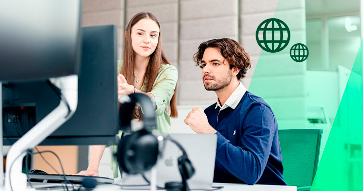 Zwei junge Menschen besprechen etwas und schauen dabei auf einen PC-Bildschirm.