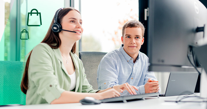 Zwei junge Menschen besprechen etwas und schauen dabei auf einen PC-Bildschirm.