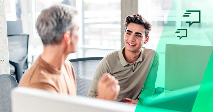 Ein erfahrener Mitarbeiter führt Gespräch mit einem jungen Mann in einem hellen Büro.