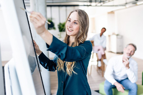 Eine Frau im Besprechungsraum mit anderen Personen arbeitet am FlipChart