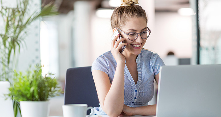Frau telefoniert und blickt in einen Laptop