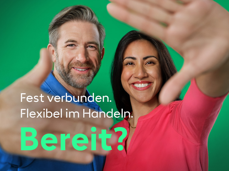 Zwei Menschen blickt lächelnd in die Kamera und streckt die Hände einladend nach vorn.