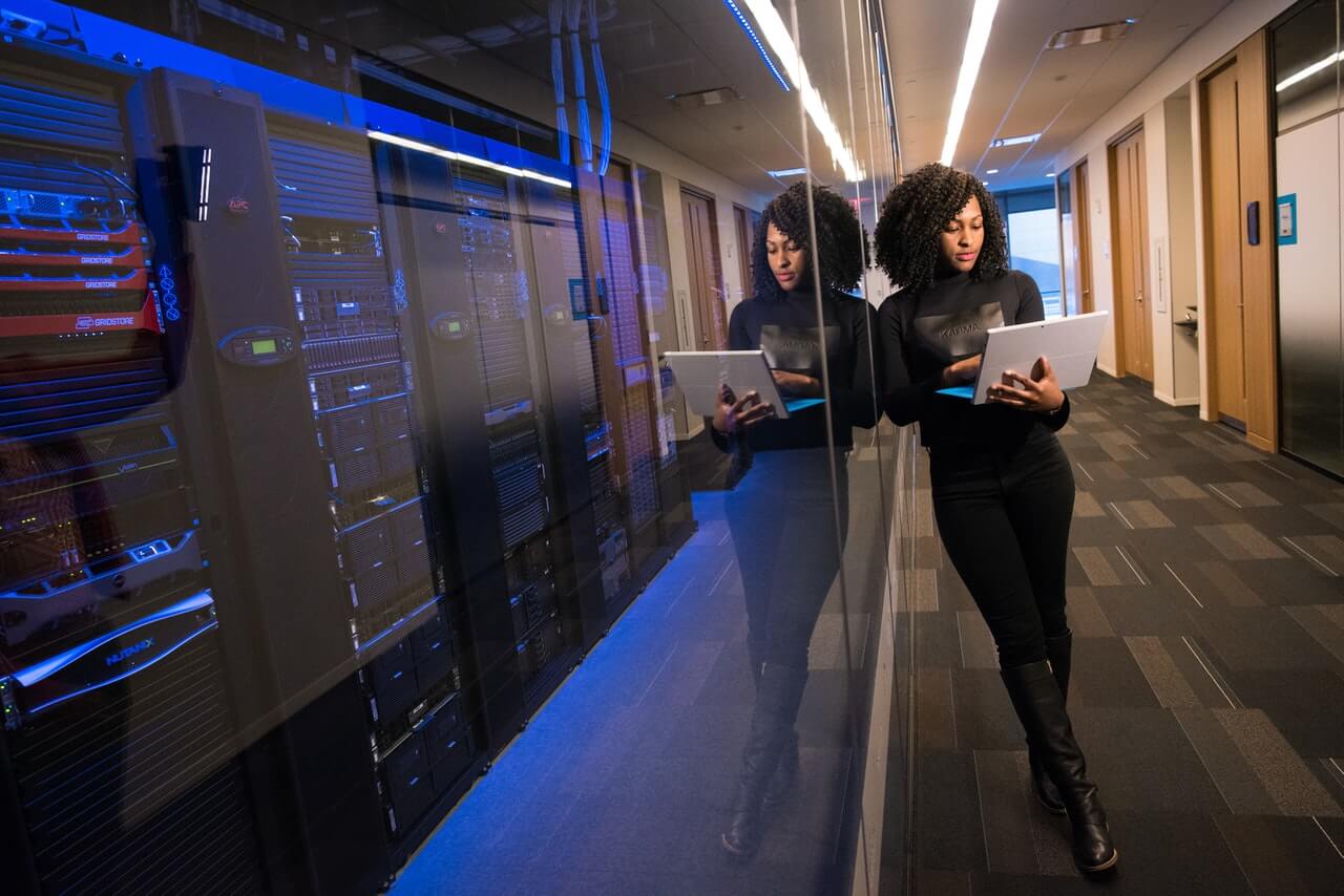 Woman with a laptop standing in front of a serverroom.