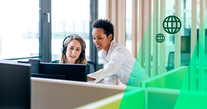Zwei Frauen besprechen etwas und schauen dabei auf einen PC-Bildschirm.