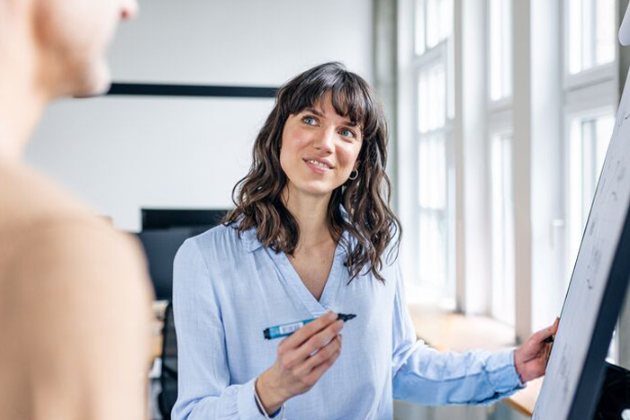 Eine Frau im Besprechungsraum mit anderen Personen arbeitet am FlipChart